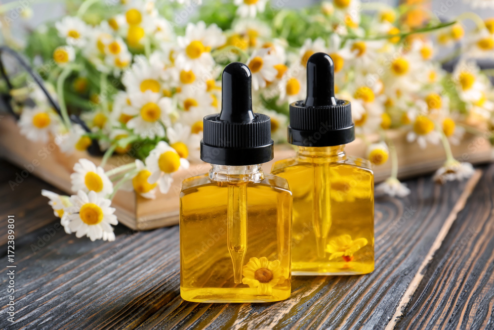 Bottles of essential oil and chamomile flowers on wooden table Bottles of essential oil and chamomile flowers on wooden table
