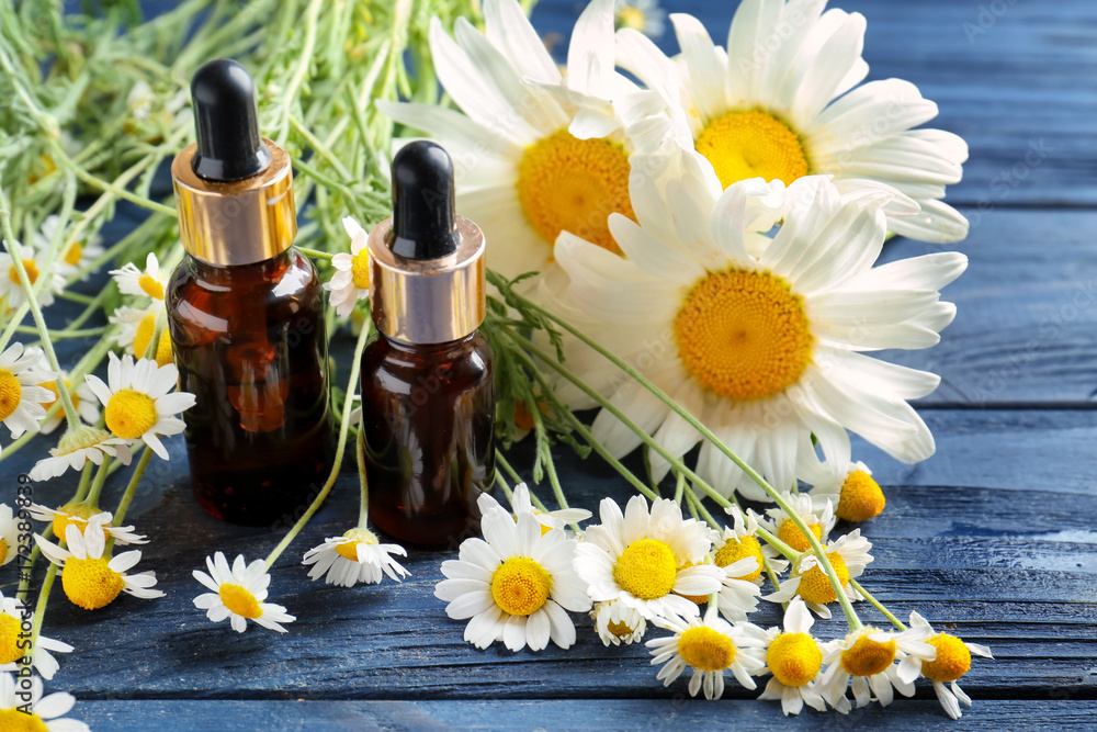 Bottles of essential oil and chamomile flowers on wooden table Bottles of essential oil and chamomile flowers on wooden table