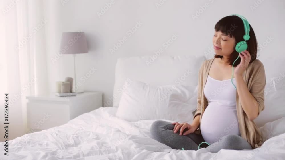 pregnant asian woman in headphones with smartphone