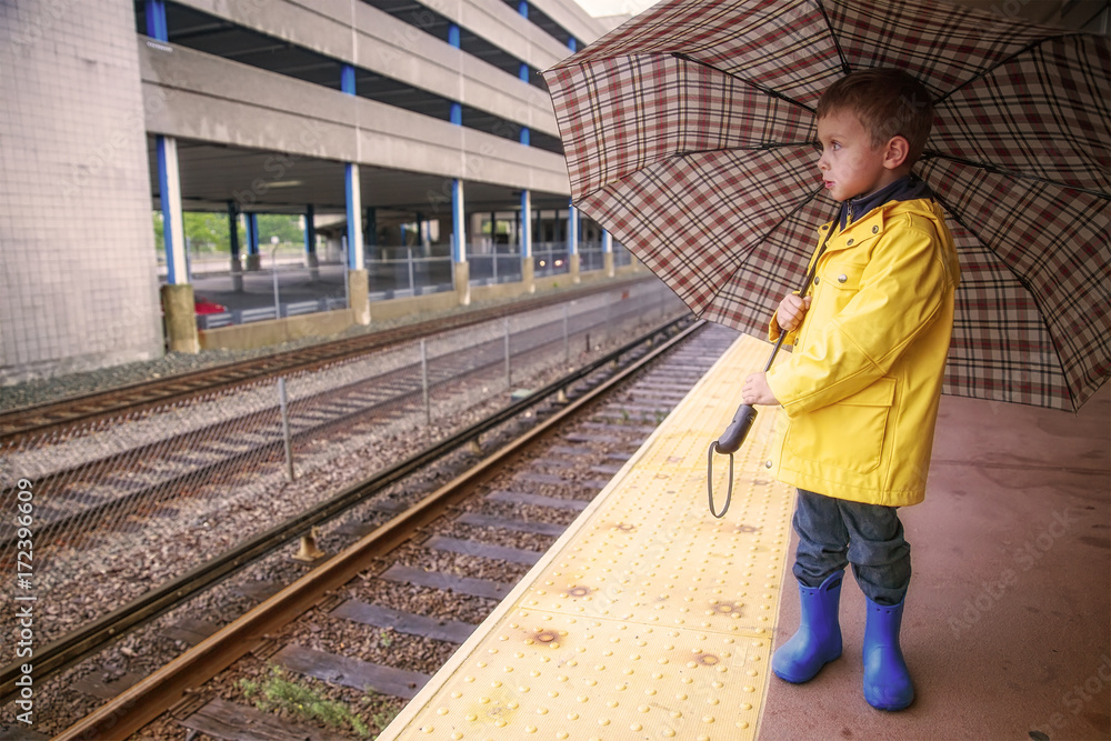 boy at the railway station in rain. cute kid in a yellow raincoat under an umbrella outside. The concept of commute. Copy space for your text boy at the railway station in rain. cute kid in a yellow raincoat under an umbrella outside. The concept of commute. Copy space for your text