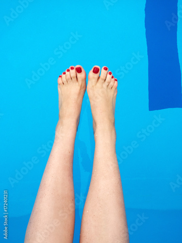 Woman's feet with red nails on the swimming pool