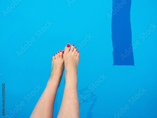 Woman's feet with red nails on the swimming pool