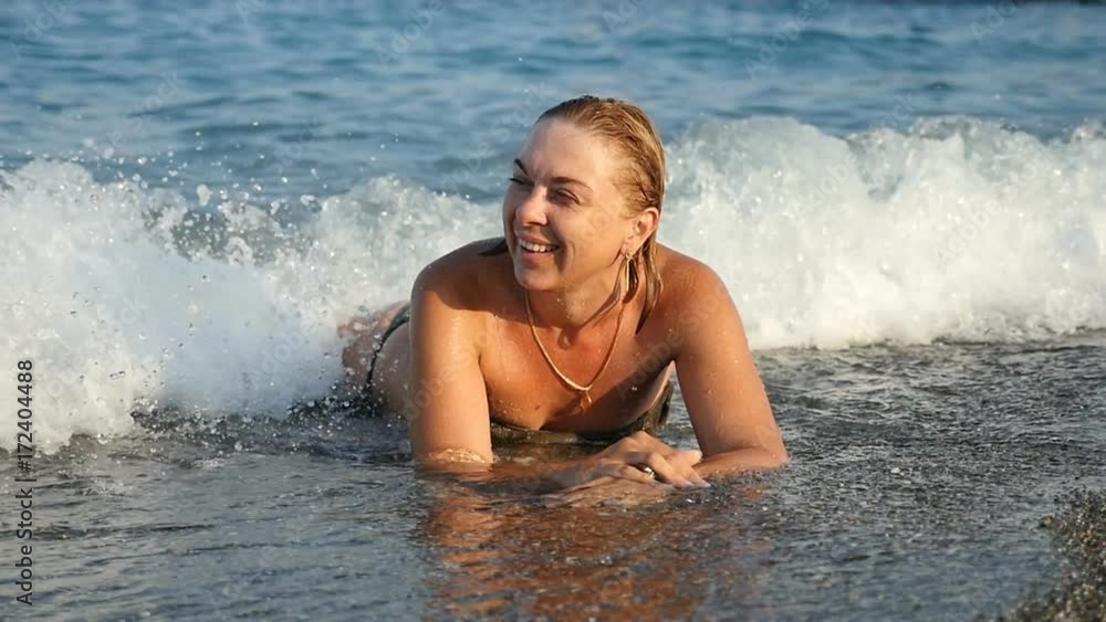 A cheerful young woman laughs and lies on a sea beach in tidying foamy waters of the Mediterranean sea and chooses shells in slow motion. The seascape is fine and impressive A cheerful young woman laughs and lies on a sea beach in tidying foamy waters of the Mediterranean sea and chooses shells in slow motion. The seascape is fine and impressive