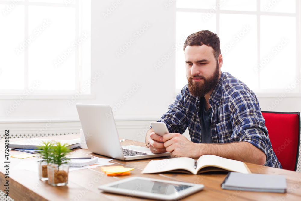 Young IT manager in office using cell phone by the laptop Young IT manager in office using cell phone by the laptop