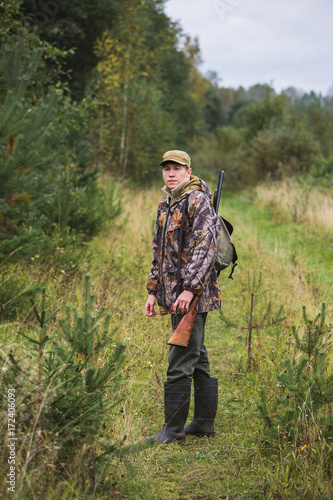 Hunter with a backpack and a hunting gun in the autumn forest. The man is on the hunt.