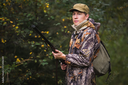 Hunter with a backpack and a hunting gun in the autumn forest. The man is on the hunt.