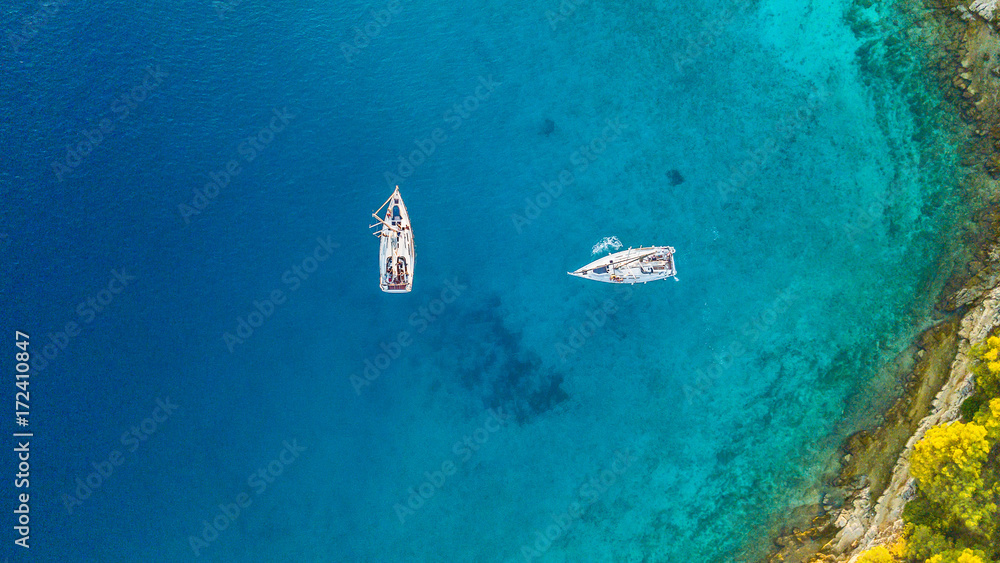Fototapeta premium Aerial view of two sailing boats anchoring next to reef