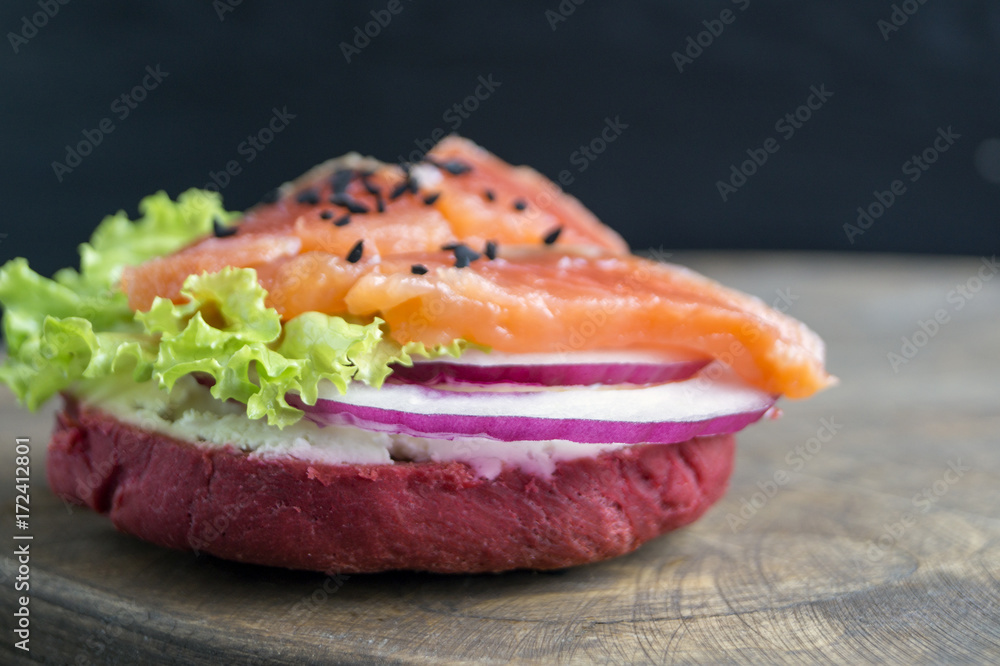 Red bun with lettuce, onion and salmon.