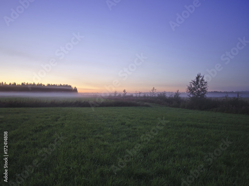 View over beautiful foggy green fields after sunset.