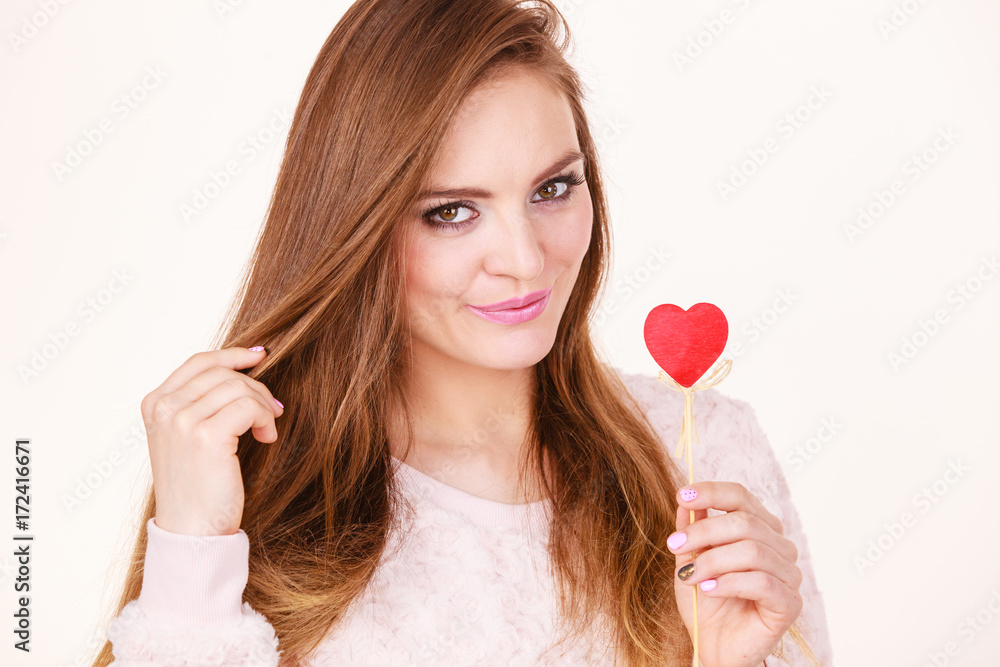 Flirty woman holding red wooden heart on stick Flirty woman holding red wooden heart on stick