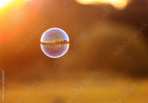 iridescent bubble with the mirrored landscape is flying to the sunset over su...