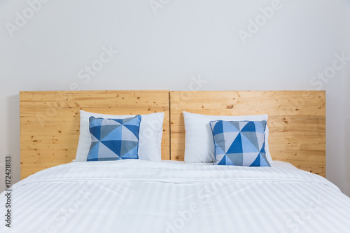 Foto empty white bed with blue and white pillows and wooden headboard in white bedroo