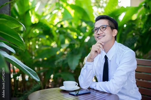 Business asian man is planning his future. He is sitting and smiling with the green nature background.