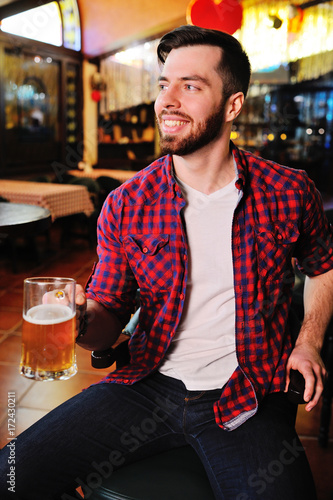 Fotografering A pub visitor drinks beer from a large beer glass while sitting on a chair