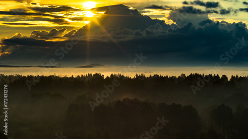 New life concept: gorgeous an promising scene of dark mountain range and foggy valley in the first rays of the sun beaming through clouds in the summer morning, golden hour