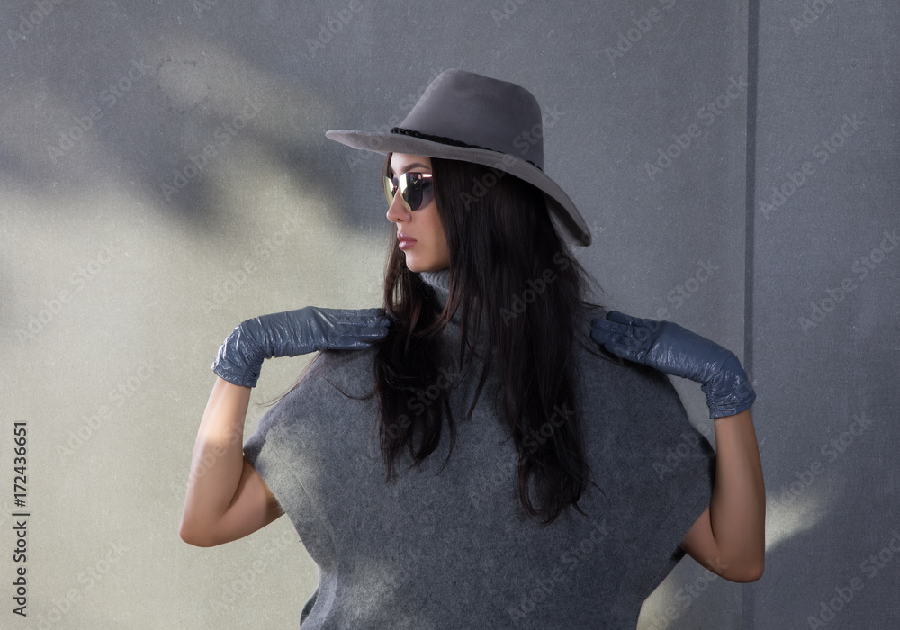 beautiful young woman in a gray sweater and gray hat on the background of a concrete wall beautiful young woman in a gray sweater and gray hat on the background of a concrete wall