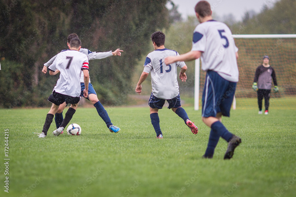 Young men playing soccer in the rain on a grass field