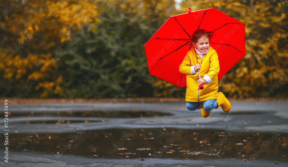 Obraz premium happy child girl with an umbrella and rubber boots in puddle on autumn walk