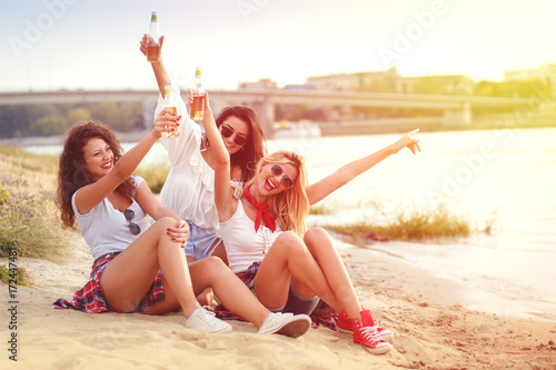 Group of young female friends sitting on the beach drinking and having fun.