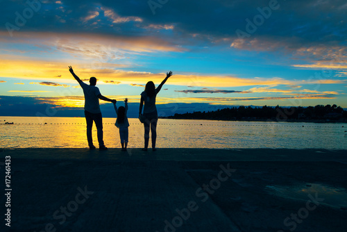 Mother, father and daughter standing at the beach looking sunset