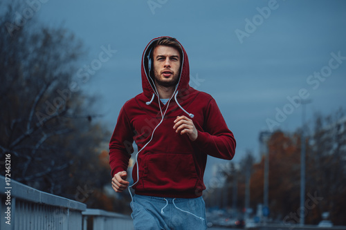 Fototapeta Naklejka Na Ścianę i Meble -  Man in red hoodie jogging beside the road in the city