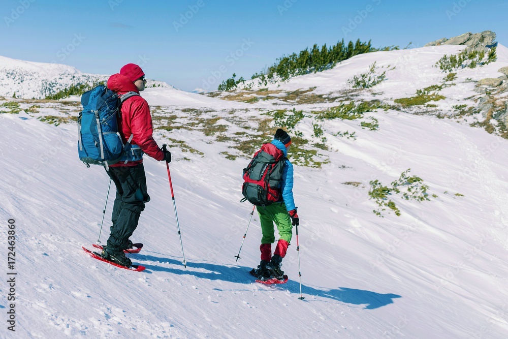 Climber with backpack trekking poles snowshoes rises to the top of the mountain in the snow on a background of beautiful blue sky.
Climber with backpack trekking poles snowshoes rises to the top of the mountain in the snow on a background of beautiful blue sky.