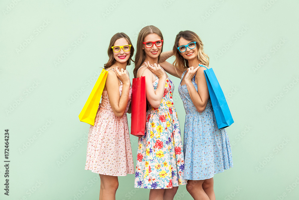 Young adult pretty womans with glasses, casual new dress with long brunette and blonde curly hair posing on green background, holds colorful shopping packages or bags Young adult pretty womans with glasses, casual new dress with long brunette and blonde curly hair posing on green background, holds colorful shopping packages or bags