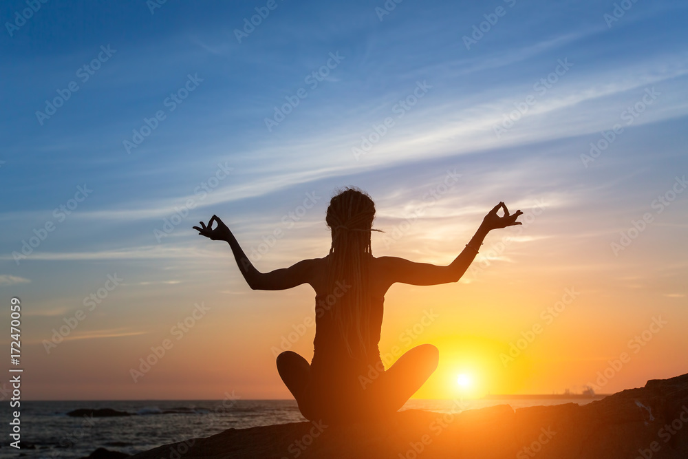 Yoga silhouette. Young woman meditation on the ocean during amazing sunset.