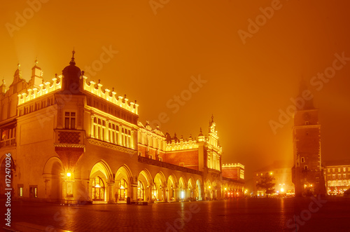 Market hall and town vity hall at main Cracow square at misty night with golden sky