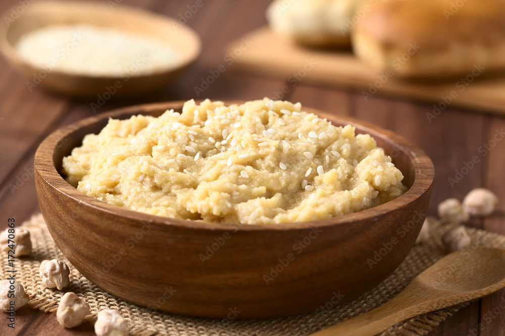 Chickpea spread or hummus with sesame seeds in wooden bowl, photographed with natural light (Selective Focus, Focus one third into the chickpea spread) Chickpea spread or hummus with sesame seeds in wooden bowl, photographed with natural light (Selective Focus, Focus one third into the chickpea spread)