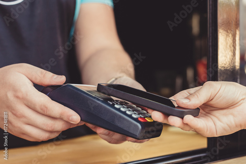 Person paying pay through smartphone using NFC technology in outdoor cafe