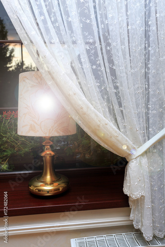 Złota lampka nocna na parapecie okna.