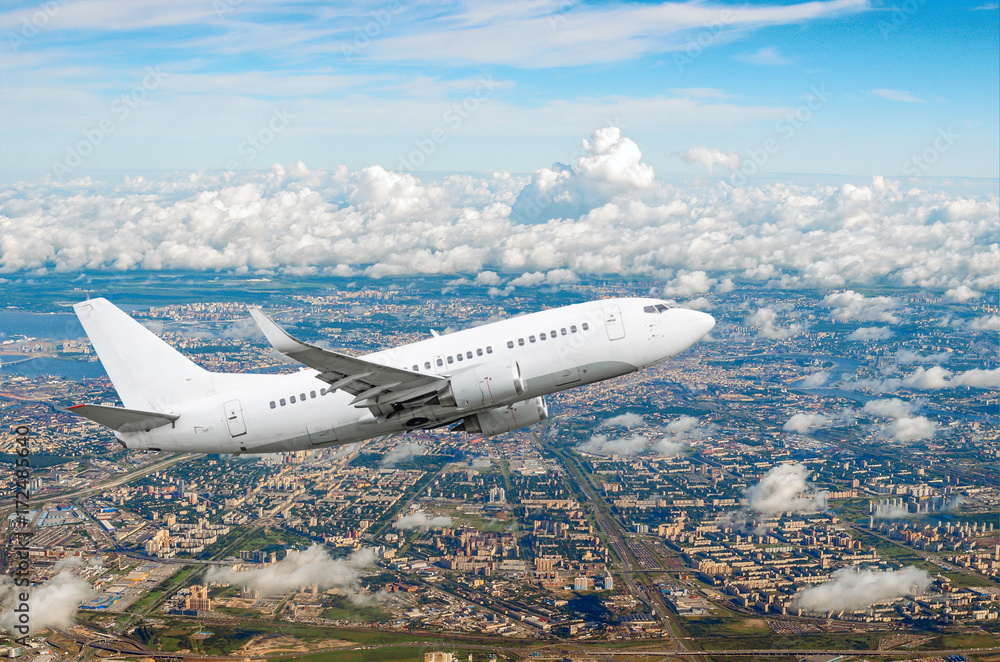 Fototapeta premium Passenger white airplane flies climbing over a large megaopolis, city