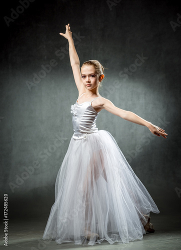 Young girl ballerina showing the dance elements on a dark background. Ballet. A little dancer.