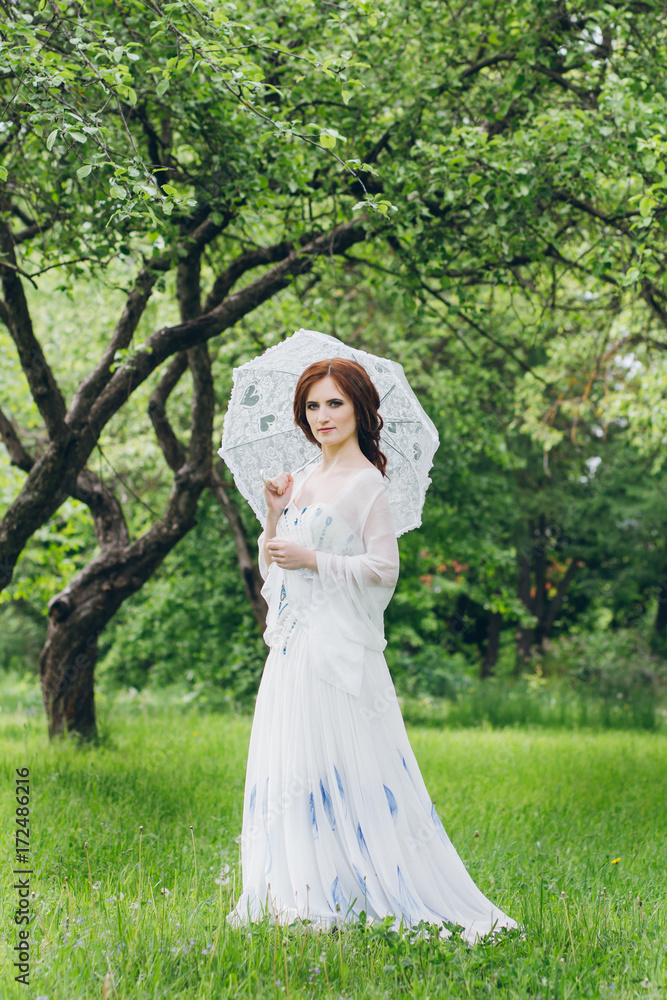 Woman in long white dress in summer garden