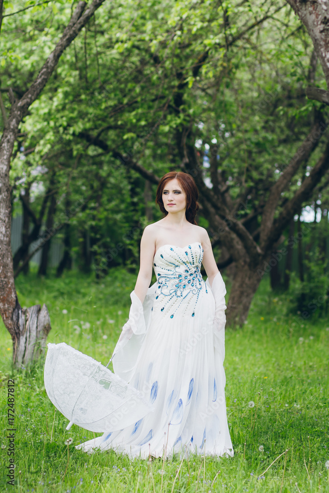 Woman in long white dress in summer garden
