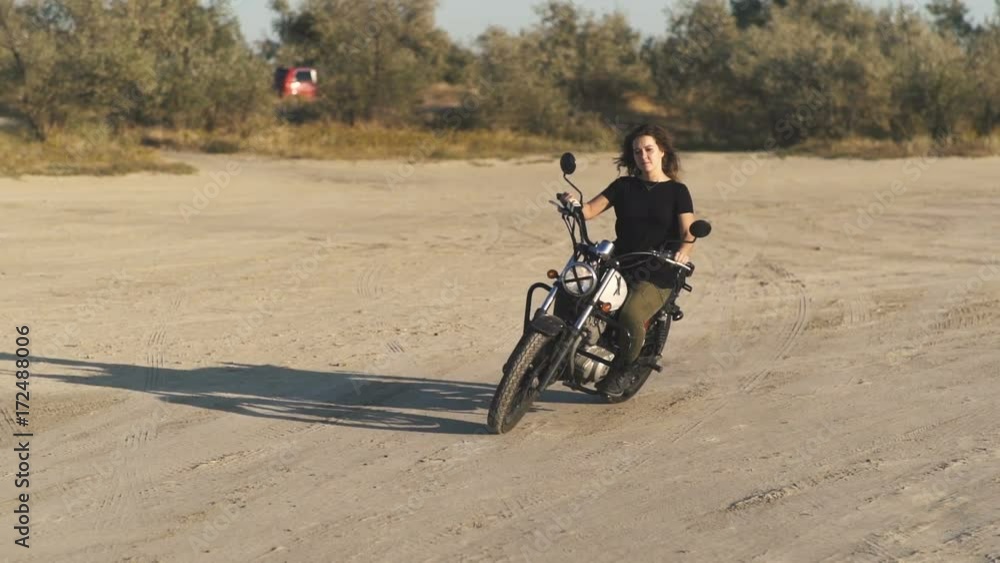  beautiful young woman riding an old cafe racer motorcycle on desert at sunset or sunrise. Female biker. Slow motion 