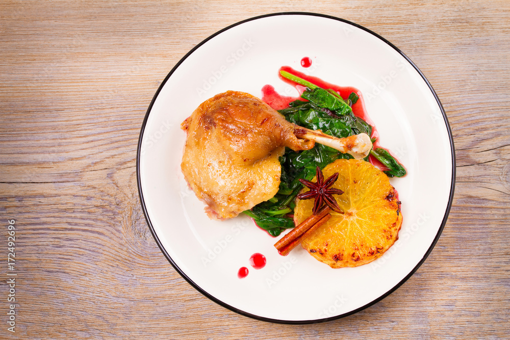 Duck leg with spinach, orange and spices: cinnamon and star anise in red wine sauce. Horizontal view from above, top shot Duck leg with spinach, orange and spices: cinnamon and star anise in red wine sauce. Horizontal view from above, top shot
