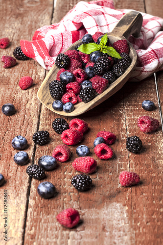 Ripe and sweet berries in a spoon on wooden background