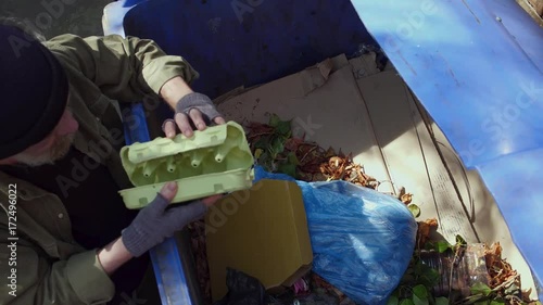 Top view of old tramp collecting empty packings from trash can. Old homeless man looking for food and other stuff in garbage.