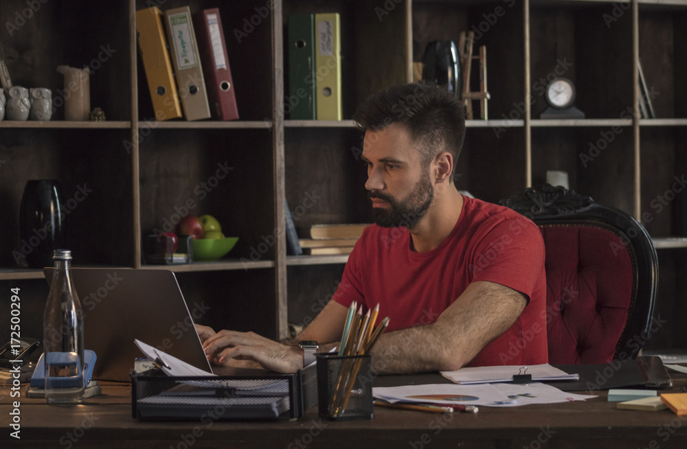 Young businessman sitting behind desk with documents and writing on laptop