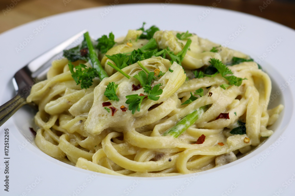 A bowl of freshly made fettuccine Alfredo with spinach and artichoke A bowl of freshly made fettuccine Alfredo with spinach and artichoke