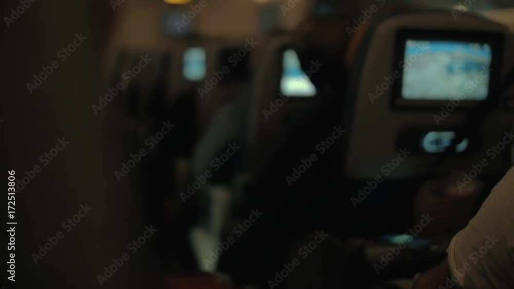 Slow motion shot of passengers following airplane route using the seat monitor map during night flight. View to the cabin with row of seats Slow motion shot of passengers following airplane route using the seat monitor map during night flight. View to the cabin with row of seats