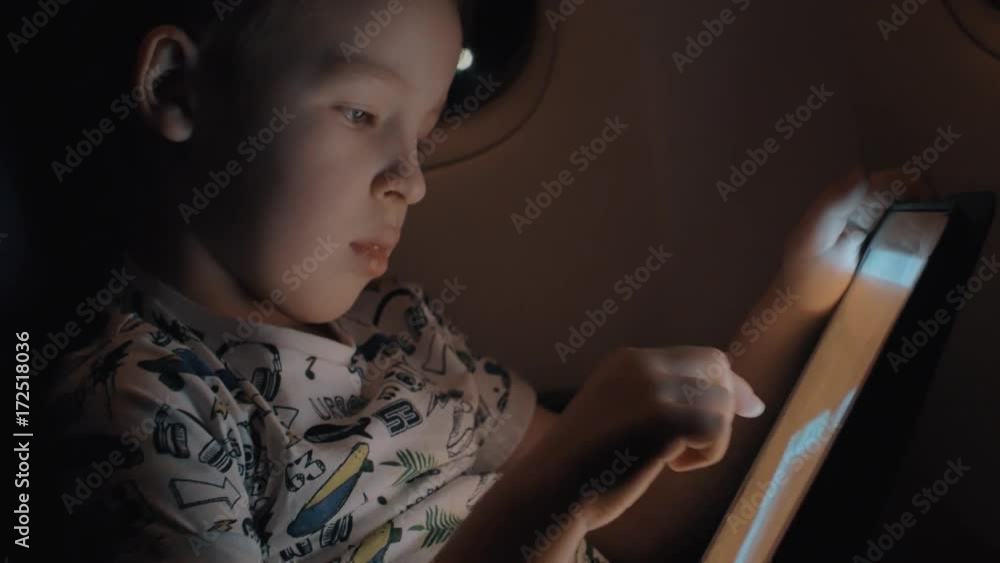 Slow motion shot of boy passenger in airplane having fun with playing on digital tablet. Entertainment during night flight Slow motion shot of boy passenger in airplane having fun with playing on digital tablet. Entertainment during night flight