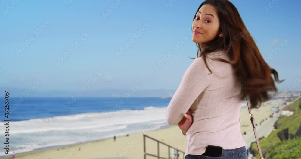 Portrait of Hispanic woman standing at the beach with arms crossed, smiling at camera. Portrait of Latina female posing with bag, touching her hair and laughing outside on beautiful summer day. 4k Portrait of Hispanic woman standing at the beach with arms crossed, smiling at camera. Portrait of Latina female posing with bag, touching her hair and laughing outside on beautiful summer day. 4k