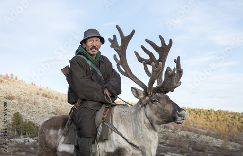 tsaatan man, dressed in a traditional deel, riding his reindeers photo