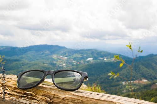 The old sunglasses , placed on wood.The background is a mountain and the sky