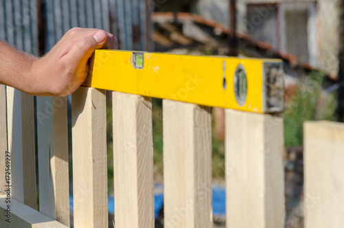 Man building a wooden fence and checking with spirit level. Close up of his hand and tool.