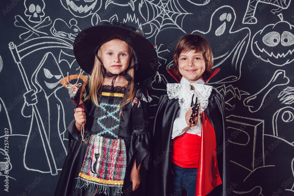 Children in scary Hallowe'en costumes stand against a wall with drawings. Witches and dracula. Children in scary Hallowe'en costumes stand against a wall with drawings. Witches and dracula.