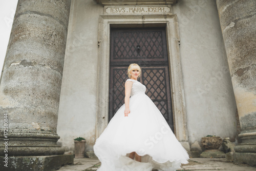 Beautiful elegant bride with perfect wedding dress and bouquet posing near old castle